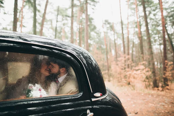 Casal de conto de fadas romântico casal beijando e abraçando na floresta de pinheiros perto de carro retro . — Fotografia de Stock