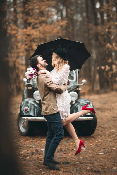 Романтическая сказочная свадебная пара целуется и обнимается в сосновом лесу рядом с ретро-машиной . — стоковое фото