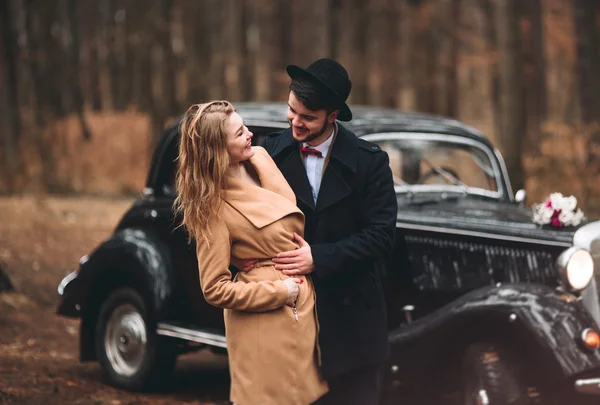 Bajki romantyczny ślub para całuje i obejmując w sosnowym lesie w pobliżu retro samochodów. — Zdjęcie stockowe