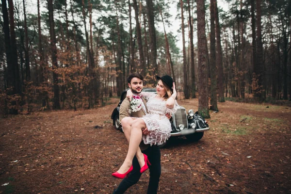 Casal de conto de fadas romântico casal beijando e abraçando na floresta de pinheiros perto de carro retro . — Fotografia de Stock