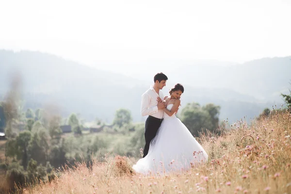 Casal de conto de fadas romântico recém-casados posando ao pôr do sol em um fundo de montanhas — Fotografia de Stock