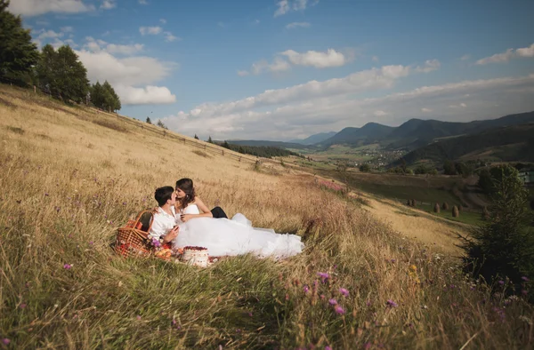 Schönes Hochzeitspaar beim Picknick mit Obst und Kuchen vor Bergkulisse — Stockfoto