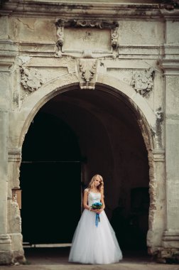 Güzel genç sarışın gelin gelin buketi ile antik kemer üzerinde duruyor