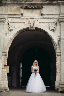 Güzel genç sarışın gelin gelin buketi ile antik kemer üzerinde duruyor