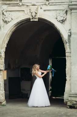 Güzel genç sarışın gelin gelin buketi ile antik kemer üzerinde duruyor