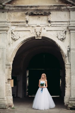 Güzel genç sarışın gelin gelin buketi ile antik kemer üzerinde duruyor