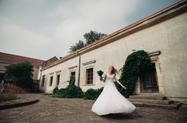 Schöne junge blonde Braut mit Brautstrauß tanzen auf dem Hintergrund wunderschöne Pflanzen — Stockfoto