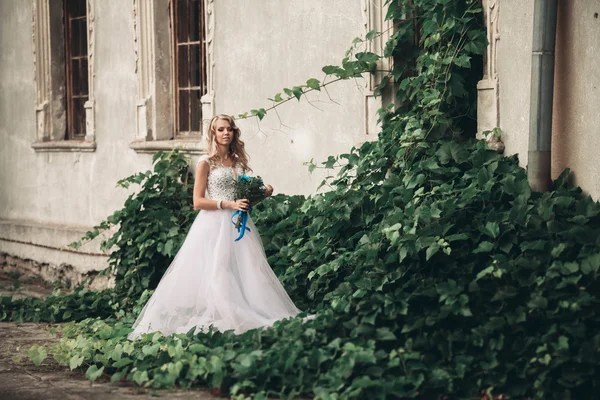 Joven novia rubia de lujo con ramo de novia posa en el fondo hermosas plantas — Foto de Stock