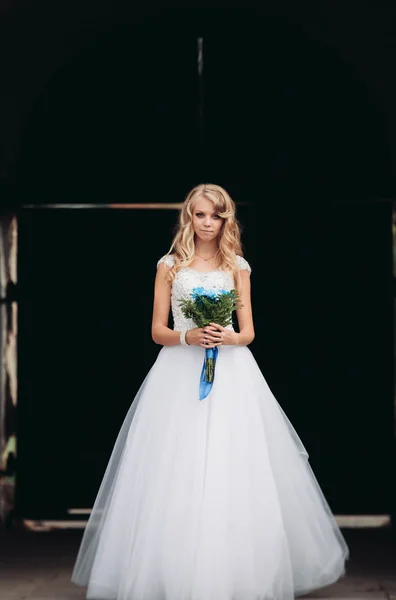 Красивая молодая блондинка с свадебным букетом стоит над древней аркой — стоковое фото