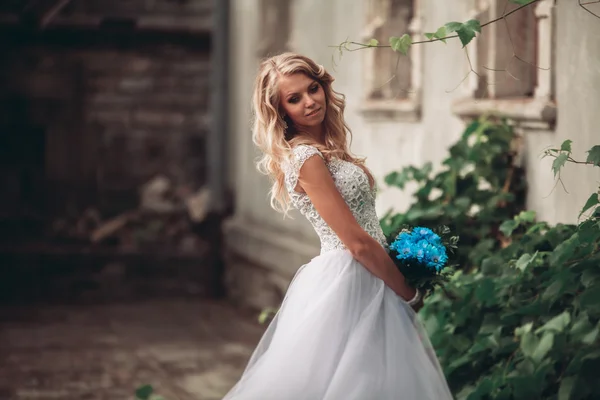 Lusso giovane sposa bionda con bouquet da sposa posa sullo sfondo splendide piante — Foto Stock