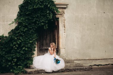 Güzel genç sarışın gelin gelin buketi arka plan güzel bitkiler merdivenlerde oturan ile