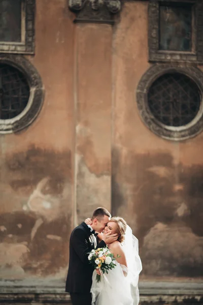 Счастливая роскошная свадебная пара стоит и целуется на улицах старого города — стоковое фото