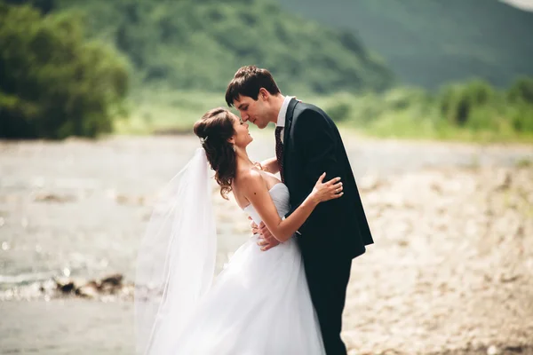 Elegante gentile sposo elegante e sposa vicino al fiume con pietre. Matrimonio coppia innamorata — Foto Stock