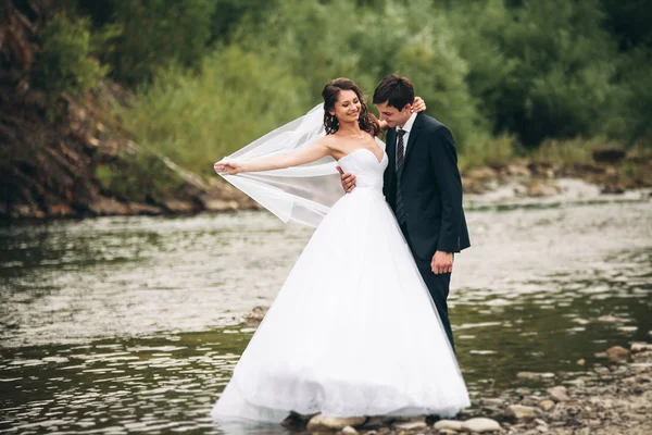 Elegant mjuka eleganta brudgummen och bruden nära floden med stenar. Bröllop par i kärlek — Stockfoto