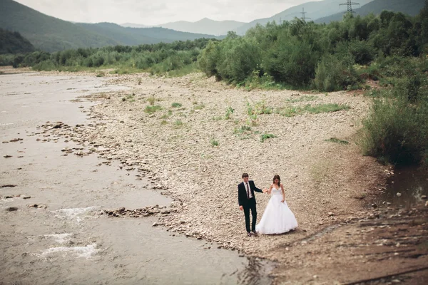 Bellissimo matrimonio coppia baciare e abbracciare vicino alla riva di un fiume di montagna con pietre — Foto Stock