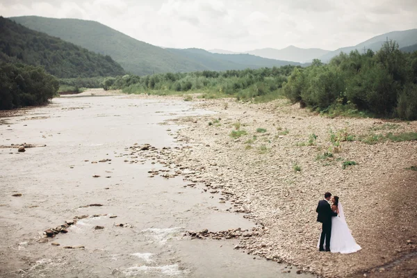 Bellissimo matrimonio coppia baciare e abbracciare vicino alla riva di un fiume di montagna con pietre — Foto Stock
