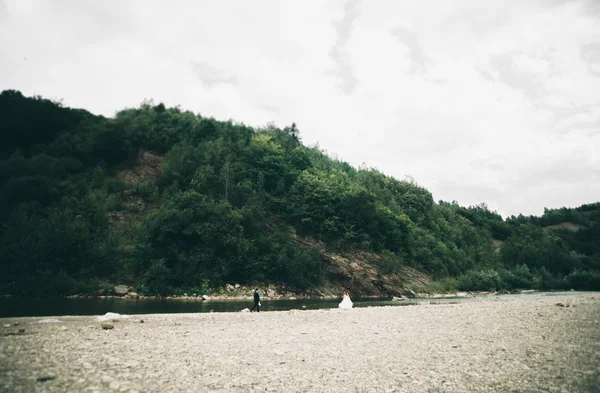 エレガントな優しいスタイリッシュな新郎と花嫁の石と川の近く。愛の結婚式のカップル — ストック写真