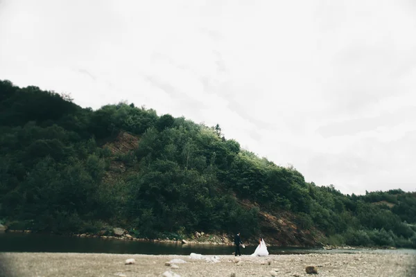 美しい結婚式のカップルのキスと石と山の川の岸の近くに抱擁 — ストック写真