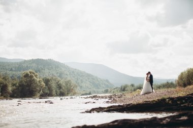 Güzel düğün çifti Nehri manzaralı dağlarda taş kalmak