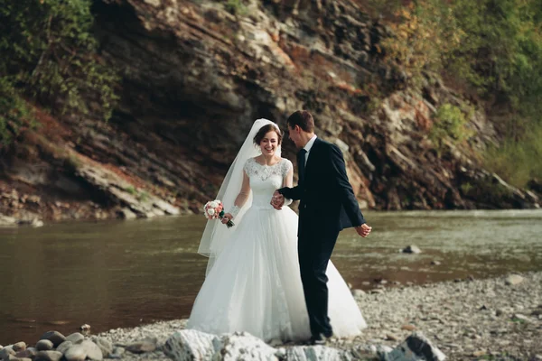 Krásný romantický ženicha a krásná nevěsta pózuje v blízkosti řeky v malebných horách — Stock fotografie