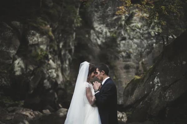 Mooie bruidspaar blijven op steen van de rivier in de schilderachtige bergen — Stockfoto