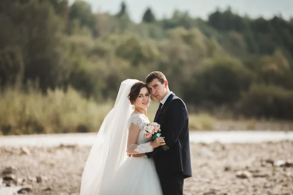 Bello sposo romantico e bella sposa in posa vicino al fiume in montagne panoramiche — Foto Stock