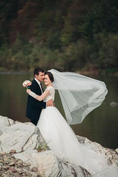 Handsome romantic groom and beautiful bride posing near river in scenic mountains — Stock Photo, Image