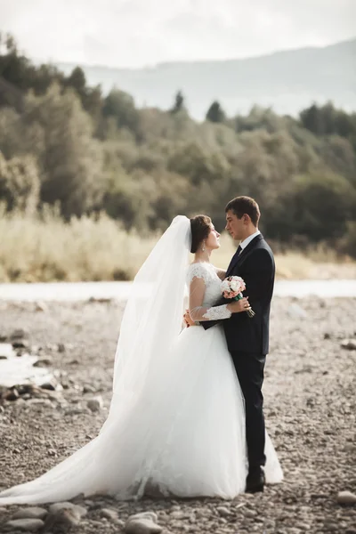 Krásný romantický ženicha a krásná nevěsta pózuje v blízkosti řeky v malebných horách — Stock fotografie