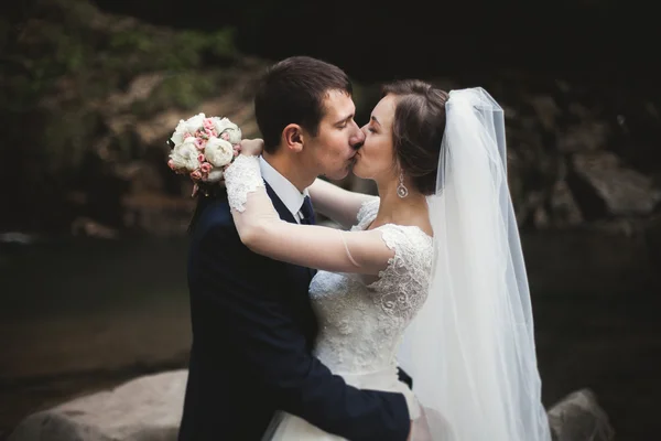 Schönes Hochzeitspaar übernachtet auf Stein des Flusses in malerischen Bergen — Stockfoto