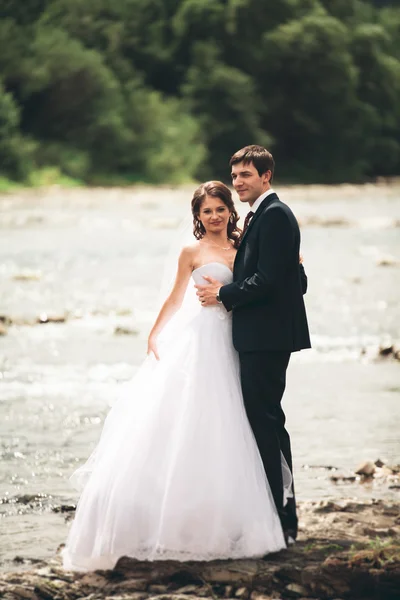 Elegante gentile sposo elegante e sposa vicino al fiume con pietre. Matrimonio coppia innamorata — Foto Stock