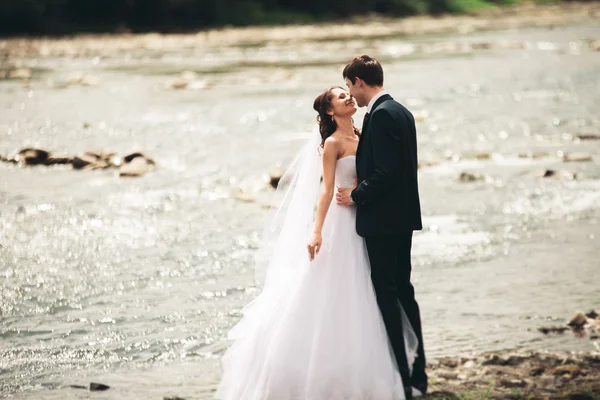 Beautifull wedding couple kissing and embracing near the shore of a mountain river with stones — Stock Photo, Image