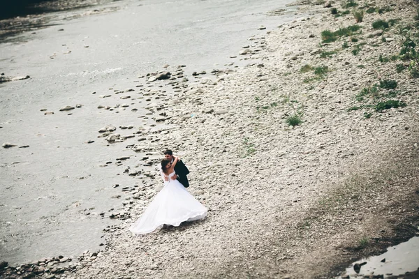 Bellissimo matrimonio coppia baciare e abbracciare vicino alla riva di un fiume di montagna con pietre — Foto Stock