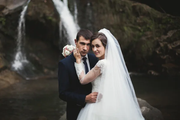 Красивая свадебная пара останавливается на камне реки в живописных горах — стоковое фото