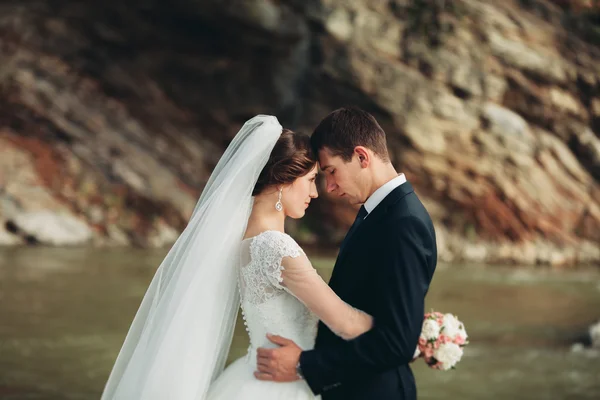 Krásný romantický ženicha a krásná nevěsta pózuje v blízkosti řeky v malebných horách — Stock fotografie