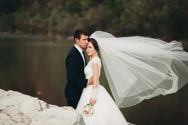 Romantikus vőlegény jóképű és pózol a festői hegyek-folyó közelében, a gyönyörű menyasszony — Stock Fotó
