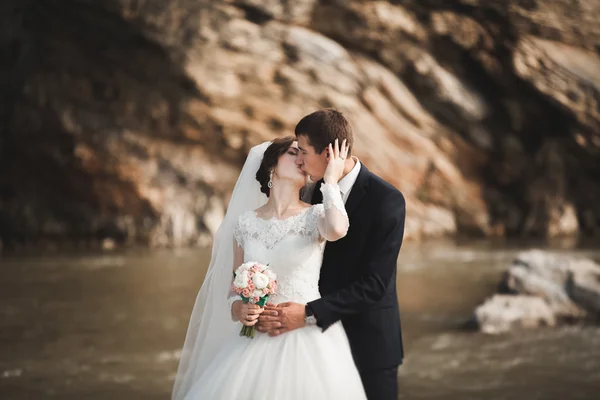 Krásný romantický ženicha a krásná nevěsta pózuje v blízkosti řeky v malebných horách — Stock fotografie
