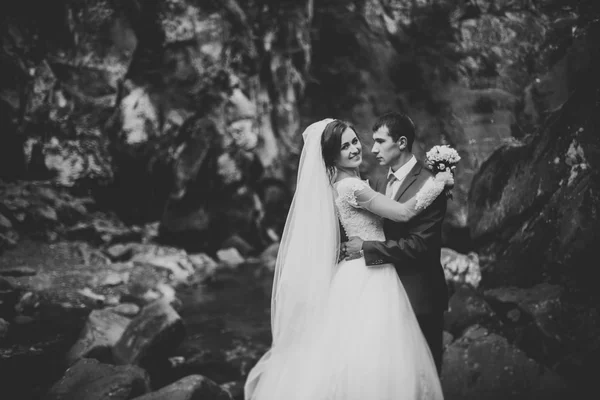 Mooie bruidspaar blijven op steen van de rivier in de schilderachtige bergen — Stockfoto