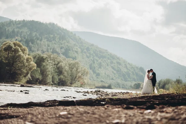 Hermosa pareja de boda estancia en piedra del río en las montañas escénicas —  Fotos de Stock