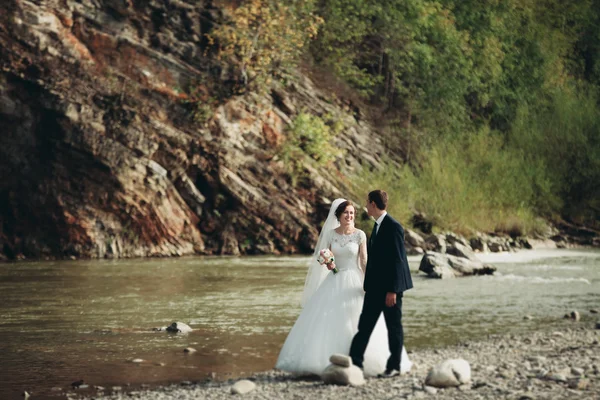 Красивый романтический жених и красивая невеста позируют у реки в живописных горах — стоковое фото