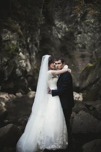 Красива весільна пара залишається на камені річки в мальовничих горах — стокове фото