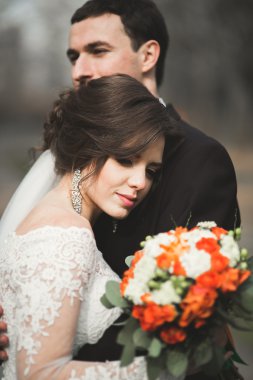 Şık bir çift yeni evliler düğün günlerinde ellerinde buketle parkta yürüyorlar.