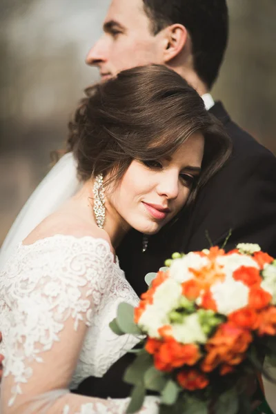 Elegante pareja de recién casados felices y elegantes caminando por el parque en el día de su boda con ramo — Foto de Stock