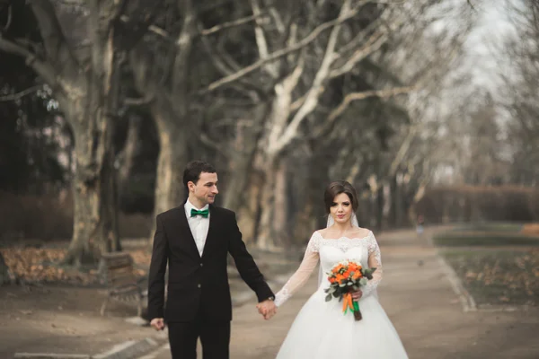 Stilvolles Brautpaar spaziert am Hochzeitstag mit Blumenstrauß durch den Park — Stockfoto