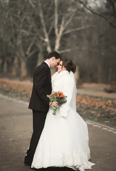 Schönes Paar von glücklichen stilvollen Brautpaaren, die an ihrem Hochzeitstag mit Blumenstrauß im Park spazieren gehen — Stockfoto