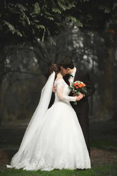Pasangan pengantin baru yang indah dan bahagia berjalan di taman pada hari pernikahan mereka dengan karangan bunga — Stok Foto