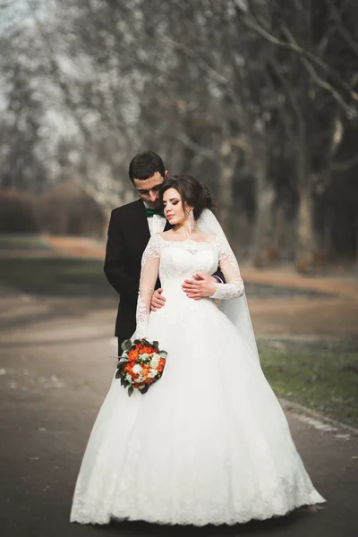 Stylish couple of happy stylish newlyweds walking in the  park on their wedding day with bouquet