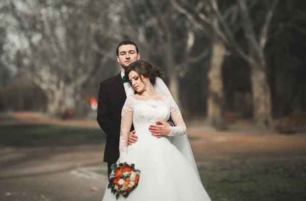 Pasangan pengantin baru bergaya bahagia berjalan di taman pada hari pernikahan mereka dengan buket bunga — Stok Foto