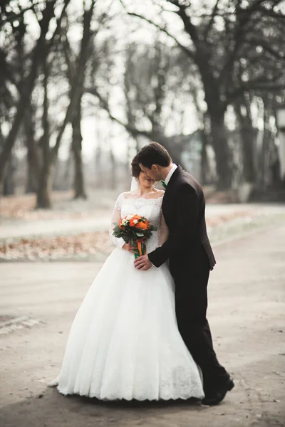 Stylový pár šťastných stylových novomanželů procházejících se v parku v jejich svatební den s kyticí — Stock fotografie