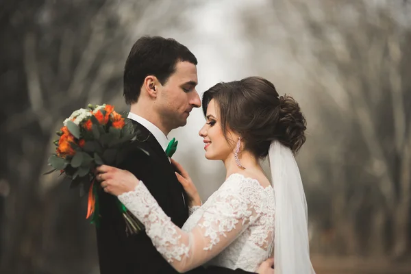 Elegante coppia di sposi felici ed eleganti che passeggiano nel parco il giorno del loro matrimonio con bouquet — Foto Stock