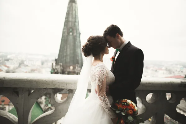 Hermosa pareja de recién casados de pie en el balcón con una vista de la ciudad — Foto de Stock